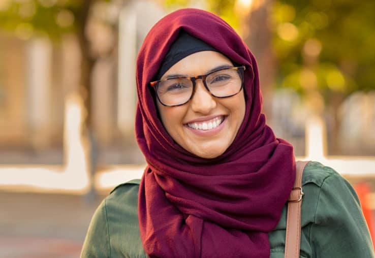 Millennial woman wearing a red hijab smiling looking at the camera.