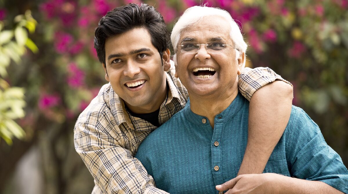 An indian son and father smiling while in a warm embrace.
