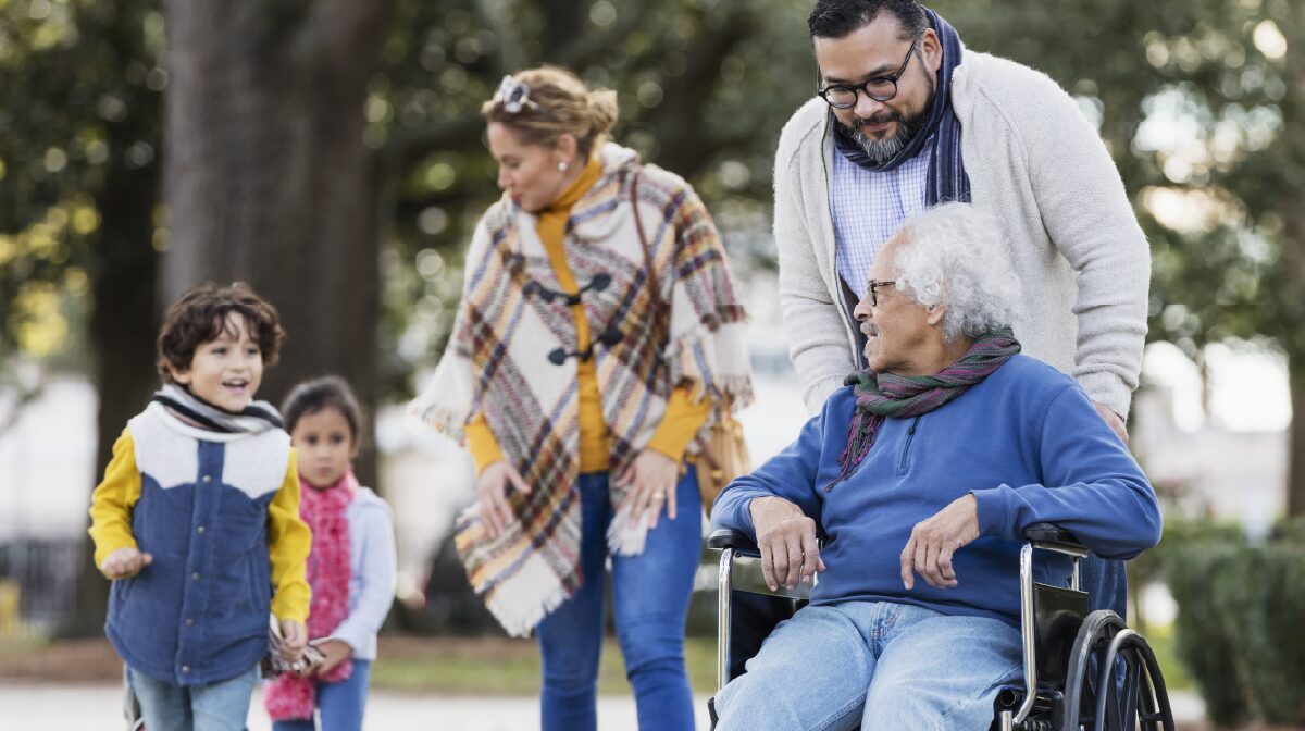 Family out for a walk together while the father pushes his dad's wheelchair.