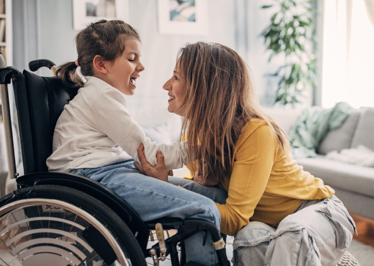Mother and her young wheel chair ridden daughter smiling at each other.