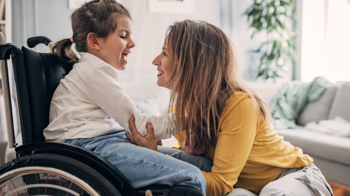 Mother and her young wheel chair ridden daughter smiling at each other during her paid leave from work.